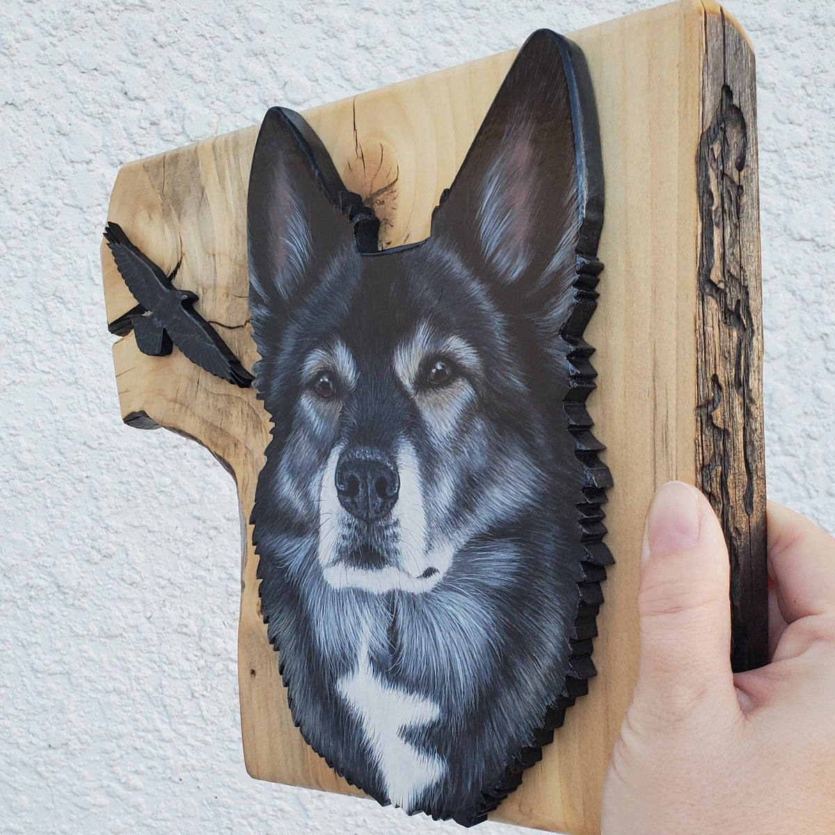 Wooden plaque with a dog painting held by a hand on a light gray background