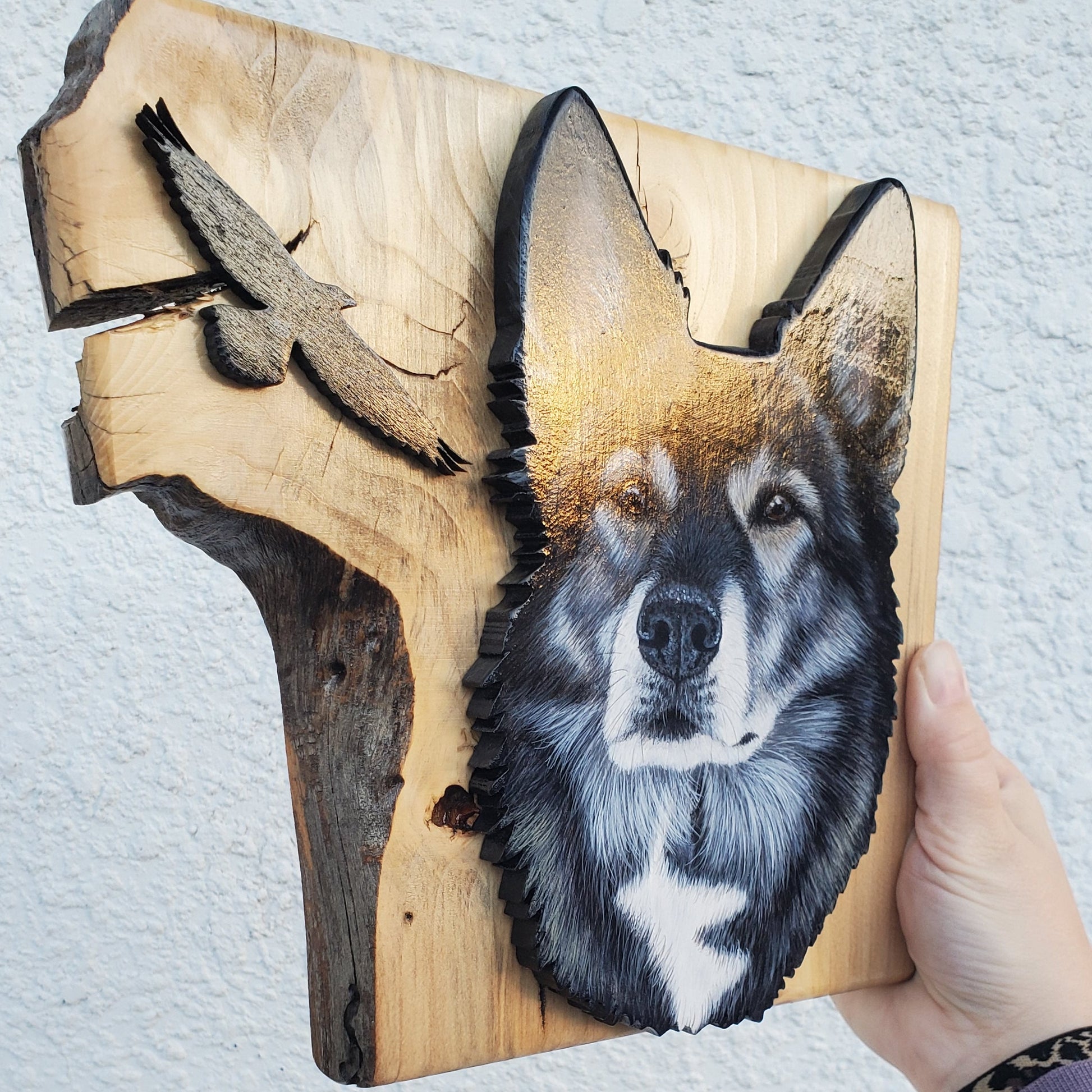 Wooden plaque with a wolf design held by a hand on a light gray background